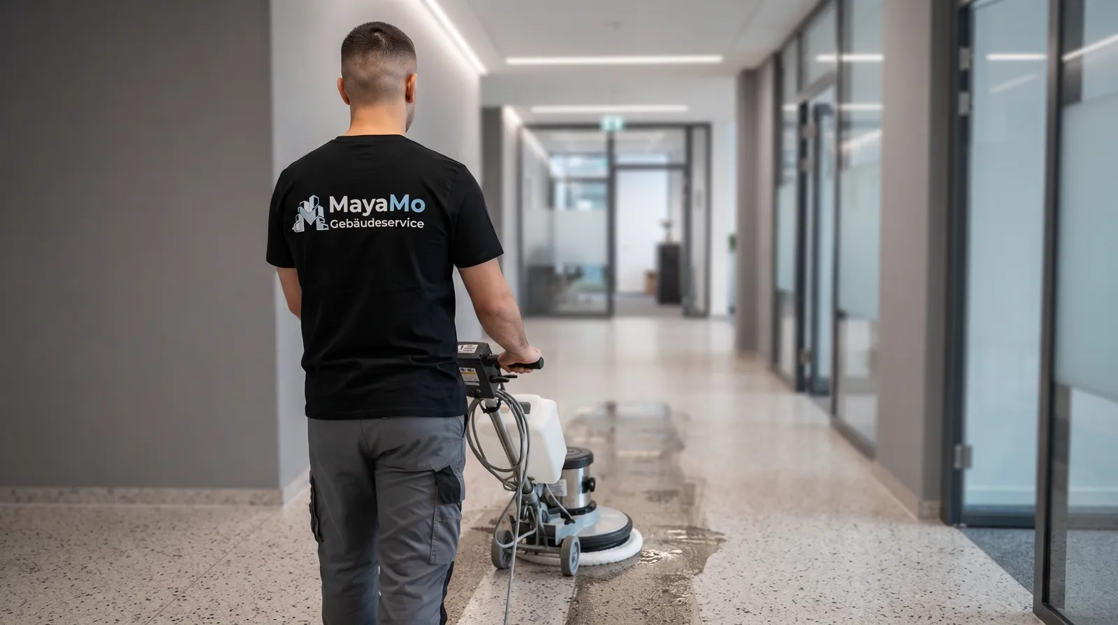 MayaMo-Mitarbeiter reinigt einen Terrazzoboden in einem Bürogang mit einer Einscheibenmaschine