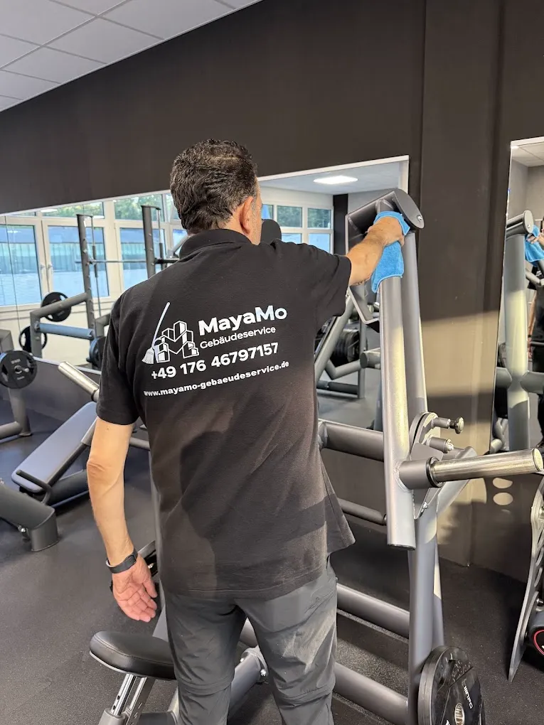 MayaMo-Mitarbeiter reinigt ein Kraftgerät in einem Fitnessstudio mit einem Mikrofasertuch
