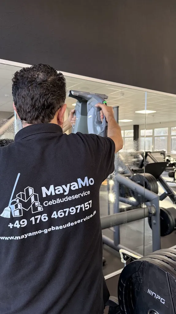 MayaMo-Mitarbeiter reinigt eine Spiegelwand in einem Fitnessstudio mit einem Fensterabzieher
